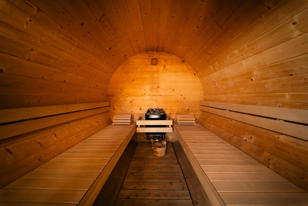 Inside the wooden barrel sauna, with warm light, benches and heater